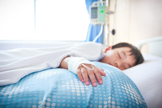 Asian boy lying on sickbed with saline intravenous (IV). 