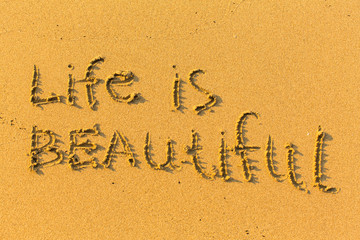 Life is beautiful - text drawn on the sand of beach.