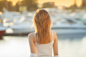 A young girl on the background of boats. Sunset in the Yacht Club. Gorgeous warm bokeh.