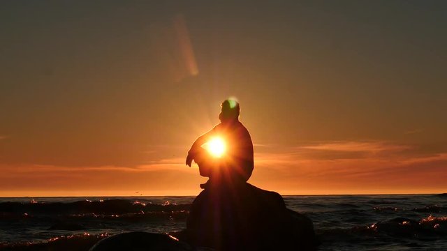 man silhouette on a rock in the sea thinking dolly shot at sunset