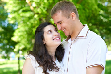 Fototapeta premium pregnant woman with husband posing in the city park, family portrait, summer season, green grass and trees