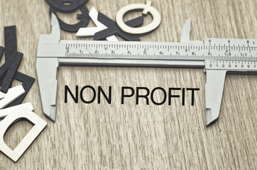 Business motivation and finance concept, vernier caliper with word NON PROFIT over wooden floor and alphabetical word made from wood background