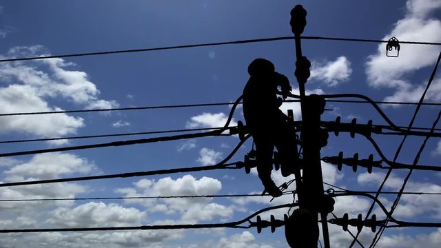 Silhouette of an electrician climbing a newly installed utility pole with blue sky background
