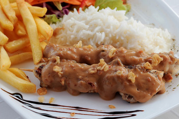 Chicken skewers on plate, garnished with sauce, rice, chips and vegetables