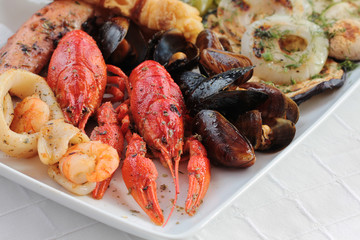 Mixed sea dish of calamari, lobster, mussels, shrimps and vegetables on plate on light background