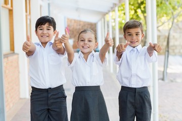 Smiling school kids showing thumbs up in corridor
