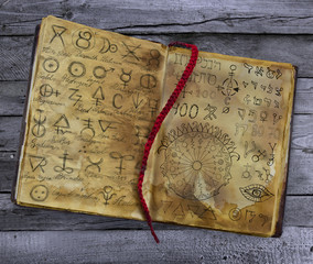 Old book with alchemic symbols lying on the wooden table