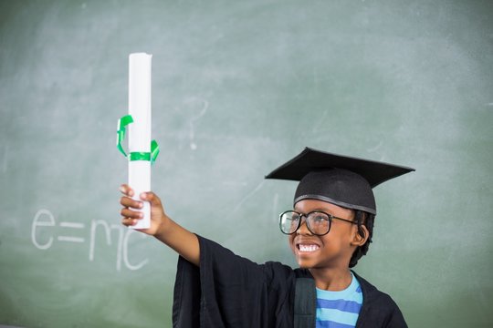 Excited schoolboy holding certificate in classroom