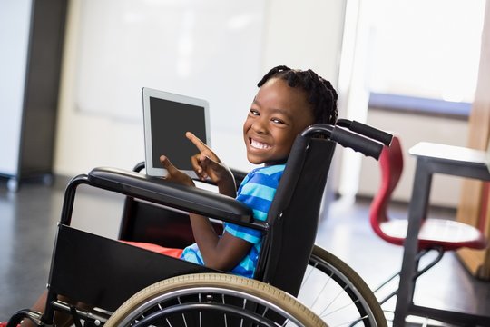Schoolboy sitting on wheelchair and using digital tablet