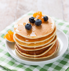 Homemade sweet pancakes with blueberries, fruit jam and honey on a white plate