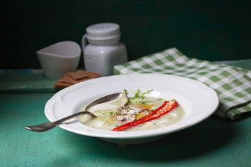 Zucchini cream soup with red pepper, cream, spices and balsamic cream on a wooden background, closeup