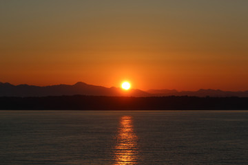 Sonne an Küste hinter Bergen hervorkommend