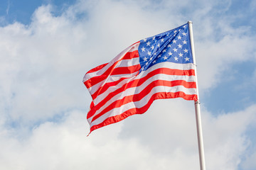 American flag waving against cloudy blue sky background.