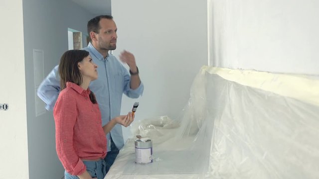Young unhappy couple painting wall at their new home and they dont like the colour, 4K
