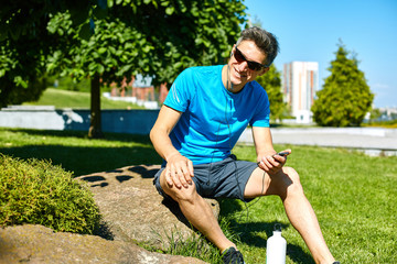 Naklejka premium athlete sitting with bottle of water and mobile phone on the stone in the park