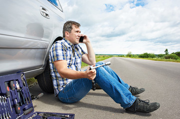 Man with phone is calling in service of spare tire car