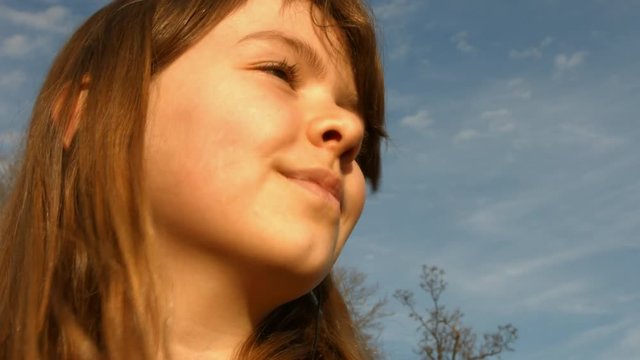 A young girl smiling and listening to music on headphones outside, in 4K