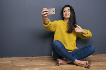 Cheerful girl making selfie against of grey wall