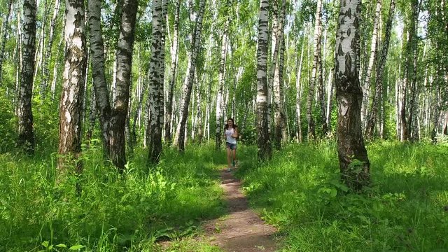 Beautiful young model girl runs in bright and beautiful birch forest. Model wears white shirt and jeans shorts. Girl runs with small chihuahua dog in slow motion using photo slider to perfectly zoom