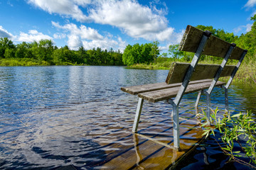 An empty bench overlooks a peaceful river, whose spring water levels have flooded the dock.