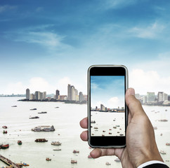 Mobile phone on hand with cityscape view and blue sky, taking photo of the city