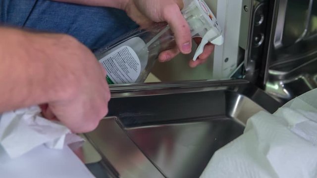 A man is having a cloth and a cleaning fluid in his hand and he is cleaning the inside of a brand new dishwasher.Close-up shot.

