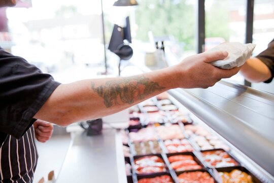 Cropped shot of butcher handing produce to customer in butchers shop