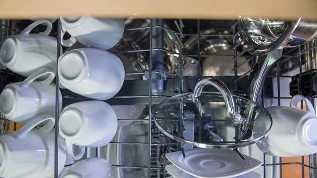 A woman is slowly closing the first and then the second shelf of a dishwasher. The device is now ready to wash. Close-up shot.
