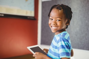 Portrait of schoolboy holding digital tablet in classroom