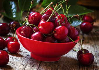 Red sweet cherry in a red bowl , dark vintage wooden background,