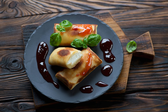 Stuffed rolled pancakes with jam, rustic wooden setting