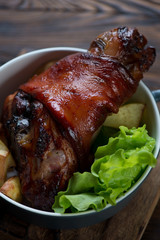 Close-up of roasted pork knuckle with green salad and potato
