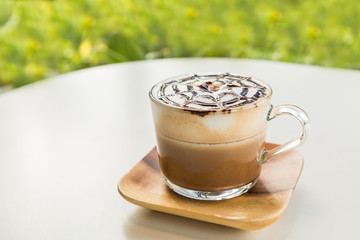 Mocha coffee (also called Caffe Mocha) with wooden saucer on white table. Interior coffee shop. Main ingredients of mocha is chocolate, espresso, hot milk (Selective focus and shallow depth of field)