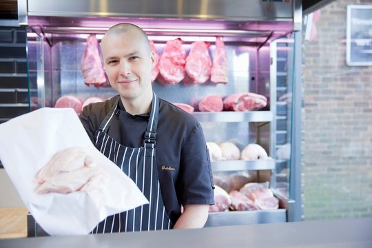 Portrait of butcher holding chicken breast in butchers shop
