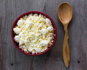 red plate with yellow fresh cheese and juniper spoon on gray old wooden table in the cracks. top view close-up