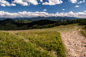 Mala Fatra mountain range from Hala na Malej Raczy mountain meadow with hiking trail and blue sky with clouds in Beskid Zywiecki mountains