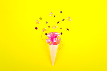 Ice cream cone with colorful party streamers on pink background. Flat lay
