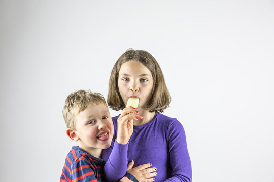 Young boy and girl sharing and eating ice cream, lovingly studio portrait. 