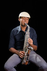 Fototapeta na wymiar With white hat a black man is sitting and playing his saxophone, dark background, nice music