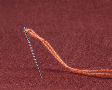 Needle anb Thread of  Yarn on the Red Felt Fabric Background Te