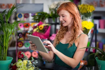 Deurstickers Bloemenwinkel Female florist using digital tablet in florist shop