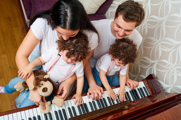 Parents with daughters twins study music at the piano. Top view