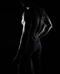 beautiful men's sporty body in backlight on the black background