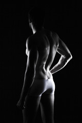 Naklejka premium beautiful men's sporty body in backlight on the black background