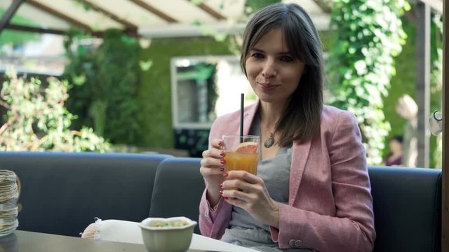 Portrait of pretty, happy young woman drinking juice in cafe in the garden
