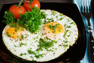 Fried eggs on a black dish served with parsley and tomatoes