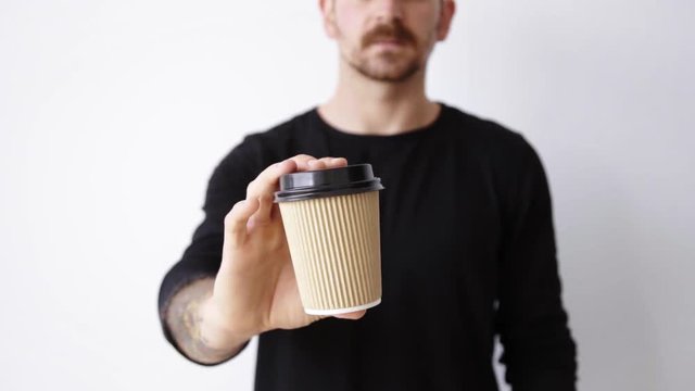 Handsome bearded in unfocused bokeh guy shows focused brown unlabeled paper cup on camera