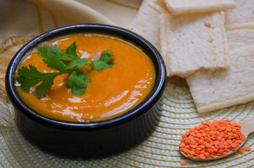 Red lentil soup with cilantro served in black ceramic bowl on wooden background.Healthy eating.