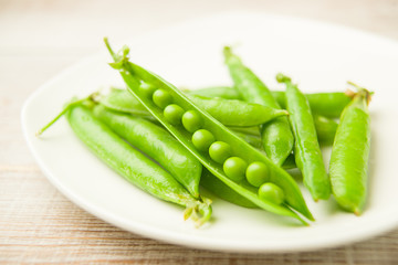 Green pea pods on the  big white plate.