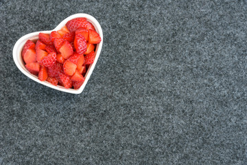 Diced strawberries in a white heart shaped bowl on a black background 
